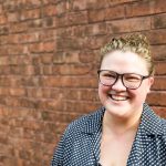 White woman with blonde hair and a wide, bright smile, her eyes squinting as she smiles